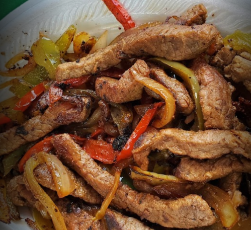A close-up of sizzling beef strips mixed with colorful bell peppers and onions on a white plate.