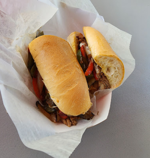 A sandwich with grilled meat, peppers, and onions, served in a toasted hoagie roll, placed in a basket with parchment paper.