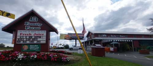 A red barn-style building with a sign for Al's Family Farms, featuring fresh juice and colorful flower beds.