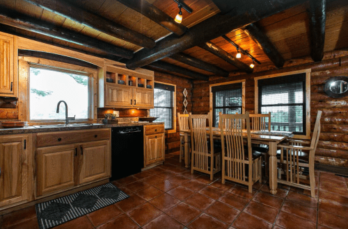 Cozy log cabin kitchen with wooden cabinets, a dining table, and large windows letting in natural light.