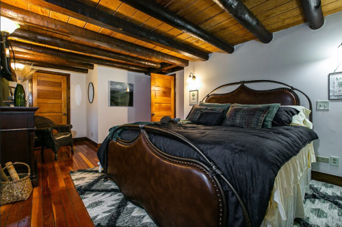 Cozy bedroom with a wooden ceiling, a large bed, and rustic decor, featuring warm lighting and wooden accents.