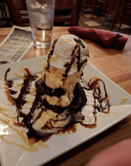 A decadent dessert featuring a brownie topped with vanilla ice cream, whipped cream, and chocolate sauce on a plate.