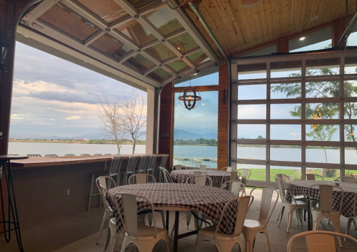Interior of a lakeside venue with tables, large windows, and a view of the water and mountains in the background.