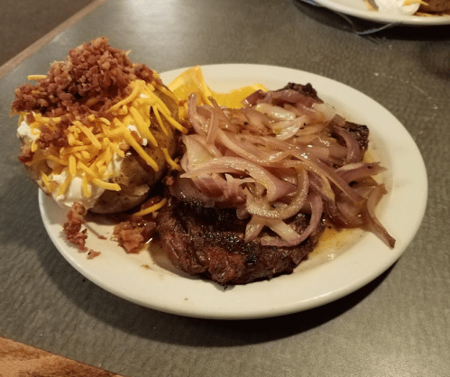 A plate featuring a grilled steak topped with onions, alongside a loaded baked potato with cheese and bacon bits.