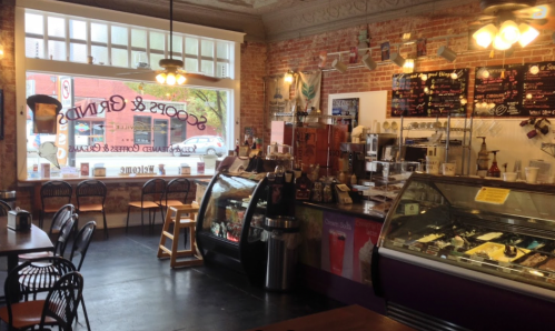 Cozy café interior with brick walls, a display case, coffee counter, and tables, inviting a warm atmosphere.