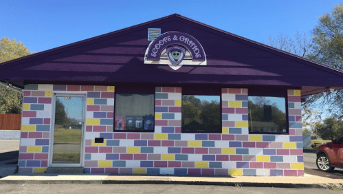 Colorful ice cream shop exterior with a purple roof and a playful mural of pastel bricks. Sign reads "Scoops & Grinds."
