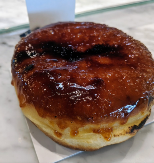 A glazed donut with a shiny caramelized topping, resting on a white paper napkin.