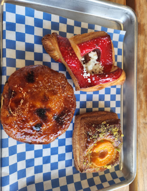A tray with three pastries: a glazed round pastry, a red fruit-filled pastry, and a pastry topped with apricot and nuts.