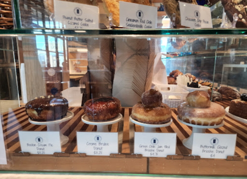 A display case with five types of donuts, each labeled with names and prices, showcasing various flavors and toppings.