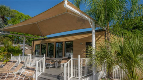 A cozy outdoor seating area with a shaded patio, surrounded by palm trees and lounge chairs.