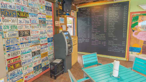 A colorful restaurant interior featuring a wall of license plates, an ATM, and a chalkboard menu.