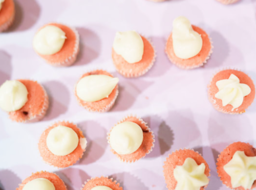 A top-down view of pink cupcakes with white frosting swirls on a light purple background.