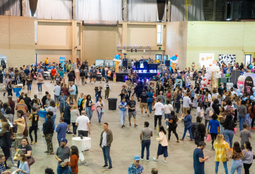 A crowded indoor event space filled with people, booths, and decorations, creating a lively atmosphere.