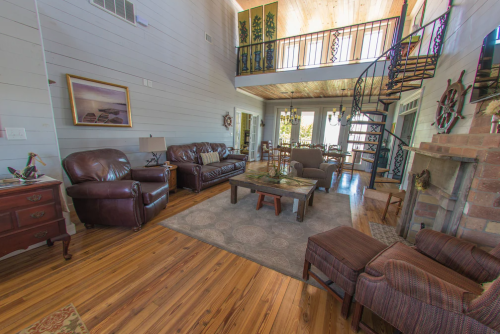 Cozy living room with leather sofas, wooden floors, a fireplace, and a spiral staircase leading to a loft area.
