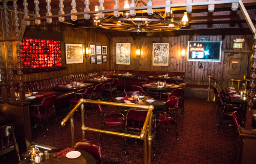 Cozy restaurant interior with wooden walls, red leather seating, and tables set for dining. Warm, inviting atmosphere.