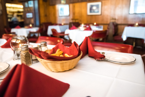 A cozy restaurant table set with red napkins, a basket of breadsticks, and condiments in a warm wooden interior.