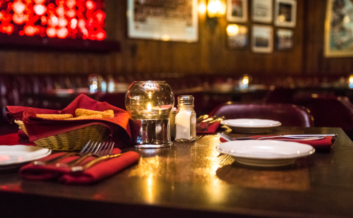 A cozy restaurant table set with red napkins, silverware, a candle, and a basket of bread, creating an inviting atmosphere.