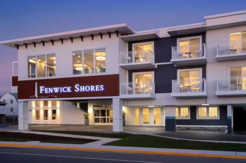Exterior view of Fenwick Shores hotel at dusk, featuring modern architecture and illuminated signage.