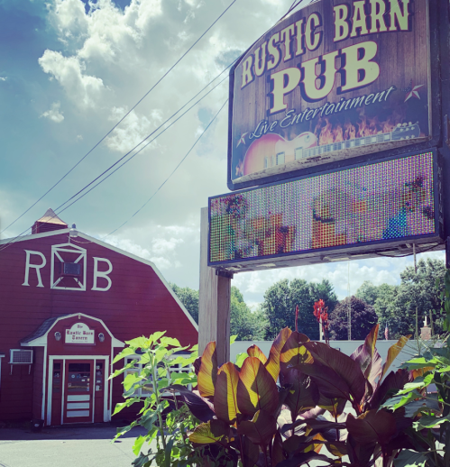 Sign for Rustic Barn Pub with colorful LED display, surrounded by greenery and a red barn in the background.