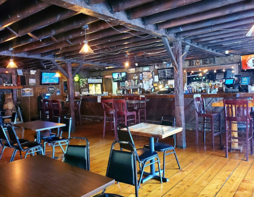 Cozy rustic bar interior with wooden beams, tables, and a well-stocked bar in the background.
