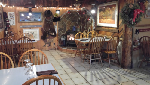 Cozy restaurant interior with wooden chairs, tables, and a stone fireplace, decorated with holiday accents.