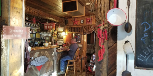 A rustic bar interior with wooden decor, a man sitting at the counter, and signs for whiskey and beer.