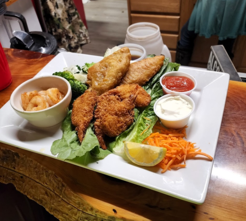 A plate of fried seafood including shrimp, fish, and sides of lettuce, carrots, and dipping sauces.