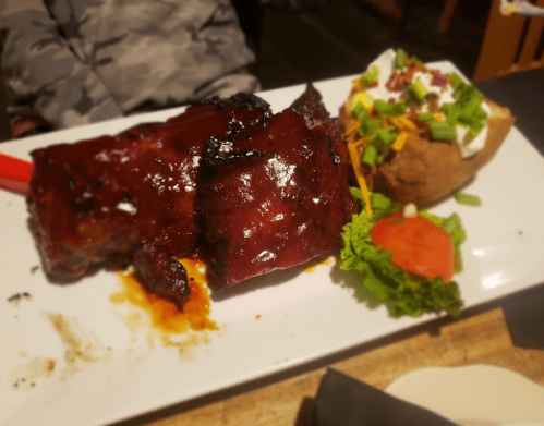A plate featuring glazed ribs, a baked potato topped with cheese and sour cream, and a side of lettuce and tomato.