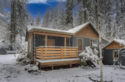 A cozy cabin surrounded by snow-covered trees, featuring a wooden porch and a serene winter landscape.