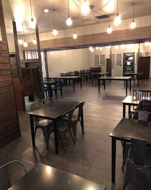 A spacious, modern restaurant interior with wooden accents, empty tables, and pendant lighting.