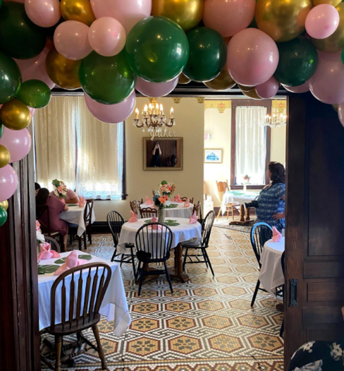 A cozy restaurant interior decorated with balloons, tables set for dining, and guests enjoying a gathering.