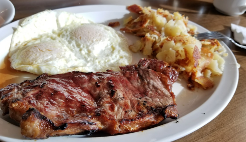 A plate with a grilled steak, two sunny-side-up eggs, and crispy hash browns.