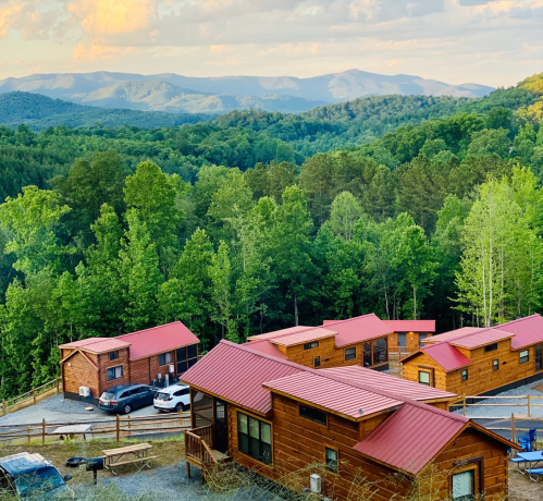 A scenic view of wooden cabins nestled among lush green trees, with mountains in the background under a cloudy sky.