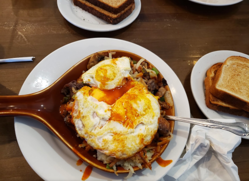 A large dish of rice topped with sautéed vegetables, beef, and two fried eggs, served with slices of toasted bread.