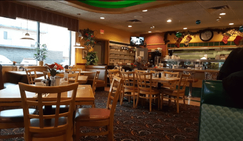 Cozy diner interior with wooden tables, chairs, and festive decorations; a few patrons and a TV in the background.