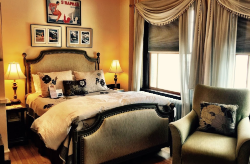 Cozy bedroom featuring a large bed, decorative pillows, armchair, and warm lighting from bedside lamps.