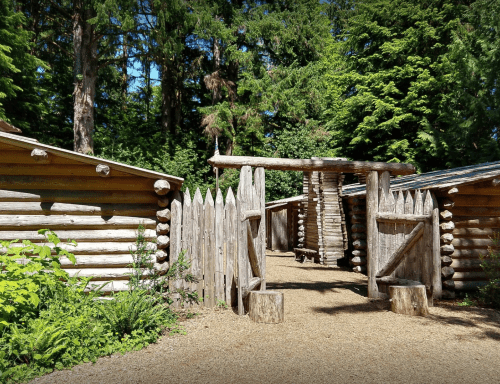 A rustic wooden structure with a gate, surrounded by tall trees and greenery, creating a serene outdoor setting.