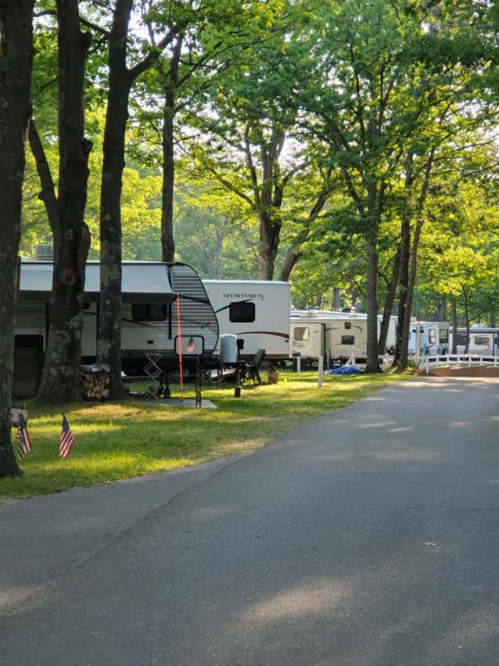 A row of RVs parked along a tree-lined road in a campground, with small American flags on the grass.