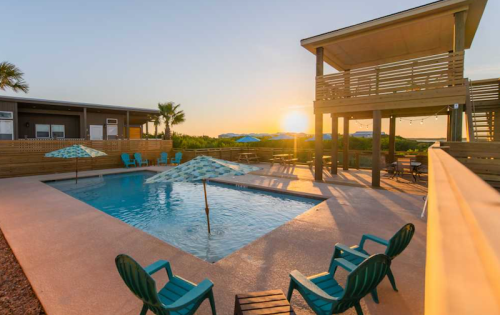 A serene pool area at sunset, featuring lounge chairs, umbrellas, and a raised deck with a scenic view.