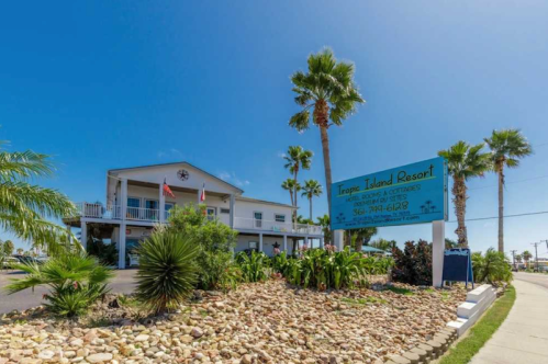 Sign for Tropic Island Resort with palm trees and landscaping under a clear blue sky.
