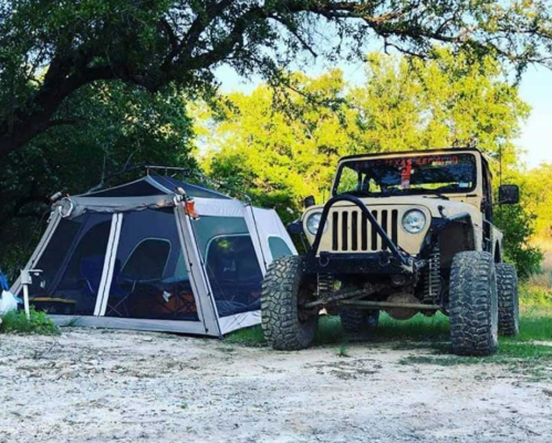 A rugged Jeep parked next to a spacious tent in a green outdoor setting.