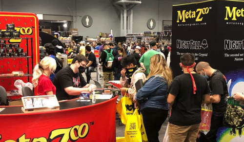 A busy convention scene with attendees at a vendor booth, some wearing masks and carrying bags.