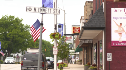 A street view featuring shops, American flags, and a street sign for N. Emmett St. on a cloudy day.