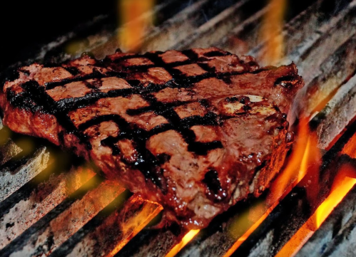 A juicy steak grilling on a barbecue, with visible grill marks and flames in the background.
