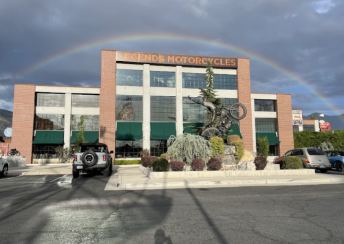 A motorcycle shop with a large statue of a biker, under a rainbow and cloudy sky.