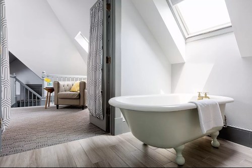 A bright bathroom featuring a freestanding tub, skylight, and a cozy seating area in a stylish attic space.