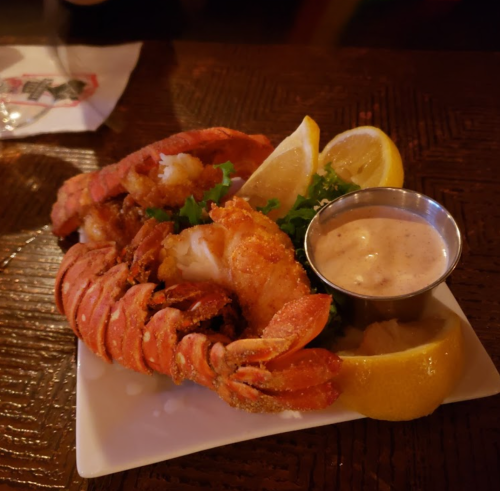A plate featuring lobster, shrimp, lemon wedges, and a small cup of dipping sauce on a wooden table.