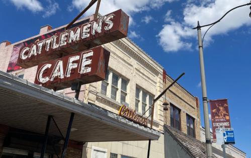 Sign for Cattlemen's Cafe in front of a historic building under a blue sky with clouds.