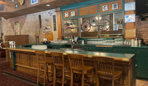 A rustic bar with wooden stools, glassware, and a mirror backdrop in a cozy, vintage setting.