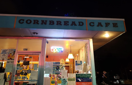 A brightly lit storefront of Cornbread Cafe at night, featuring an "open" sign and colorful decorations.